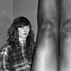 me, 20-something, sitting on a bed staring wide-eyed at the floor. In the foreground are a pair of naked legs; it looks like the subject in the foreground is standing on her head.