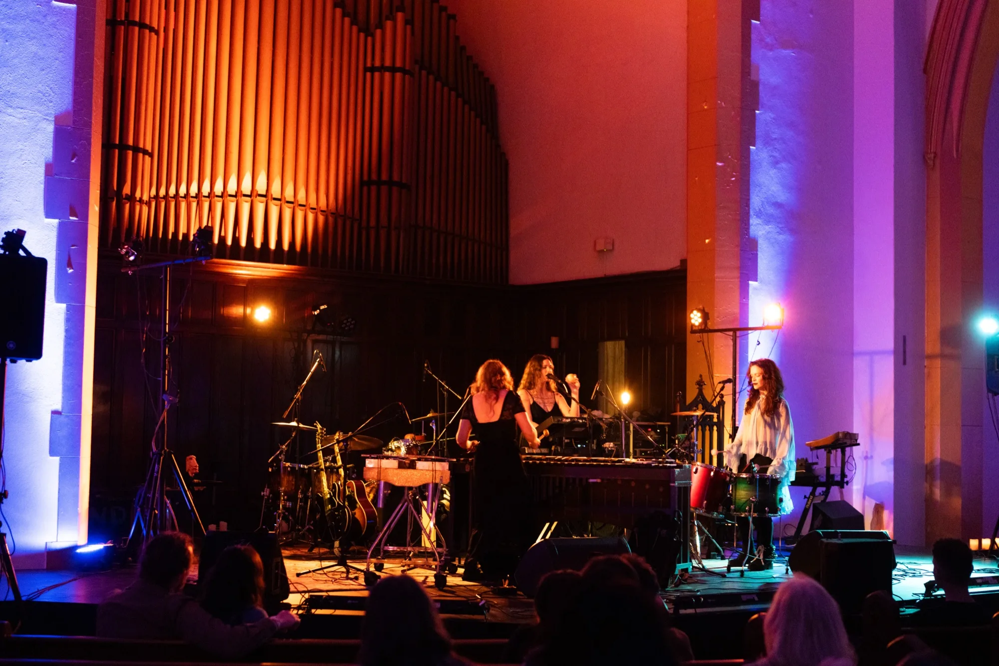 Wide shot of the band performing in front of the organ pipes, with the audience in pews in the foreground.