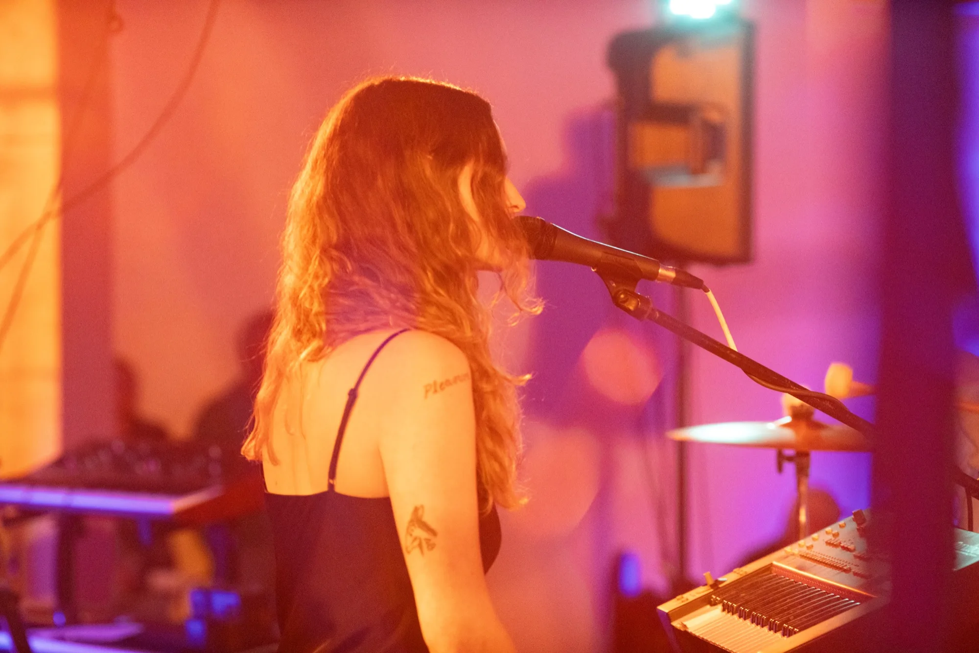 Lacey Guthrie singing into a mic in profile, a tattoo visible on her arm, under purple stage light.